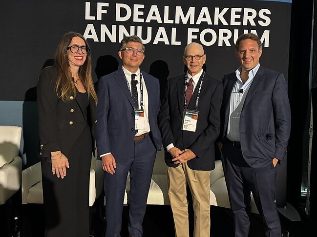 Four panelists standing on stage in front of the LF Dealmakers Annual Forum banner.
